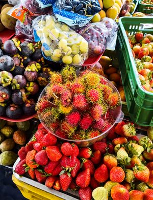 A vibrant array of tropical fruits including rambutan, strawberries, and mangosteen at a market stall.